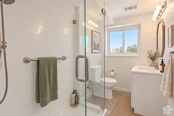 Bathroom featuring a walk-in shower with glass enclosure, subway-style wall tiling, and brushed metal fixtures, alongside a white vanity with an integrated countertop sink and an octagonal wall-mounted mirror