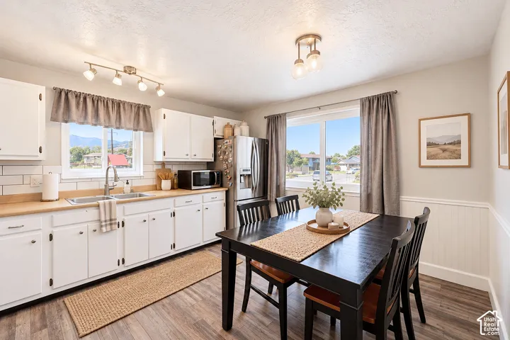 Kitchen featuring white cabinetry, wood-finish countertops, subway tile backsplash, stainless steel refrigerator, and wood-finish flooring