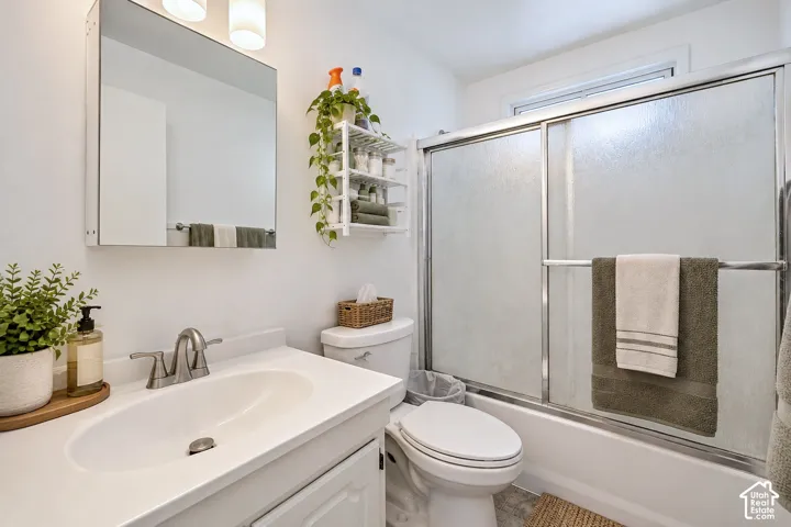 Bathroom featuring a vanity with an integrated basin, a wall-mounted mirrored medicine cabinet, dual-light overhead fixture, and a tub-shower combination enclosed by sliding glass doors
