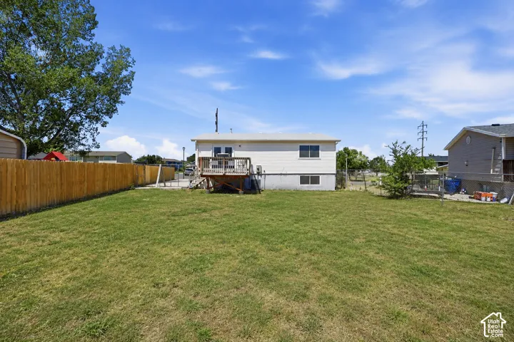 Expansive backyard featuring a large grass lawn, perimeter wood fencing, and an elevated wood deck