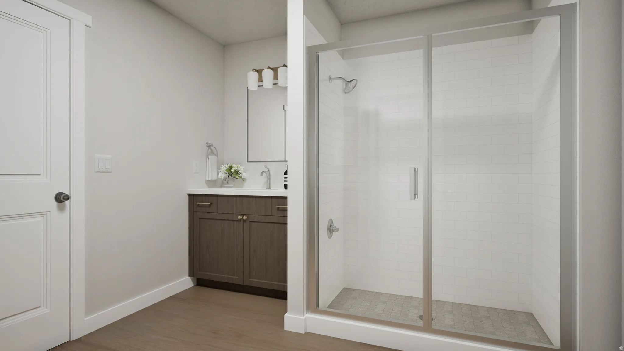 Bathroom featuring a glass-enclosed shower with white tiled walls, a wood-finish vanity with a white countertop and undermount sink, and wood-finish flooring
