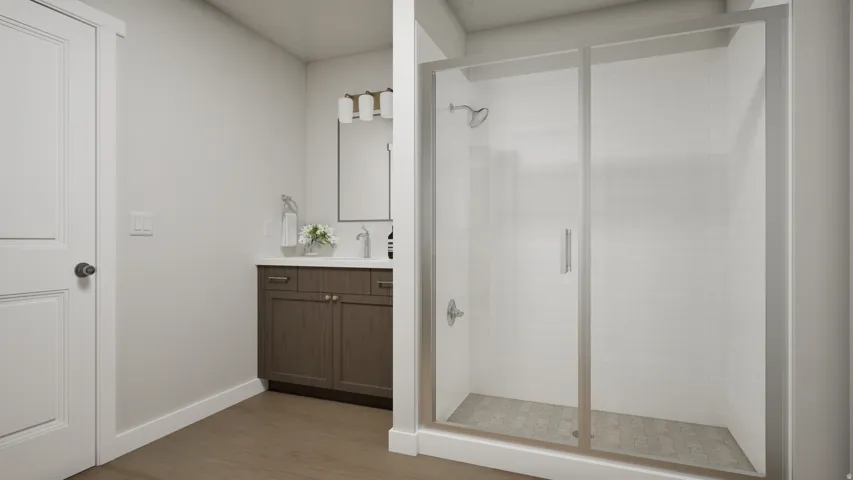 Bathroom featuring a glass-enclosed shower with white tiled walls, a wood-finish vanity with a white countertop and undermount sink, and wood-finish flooring