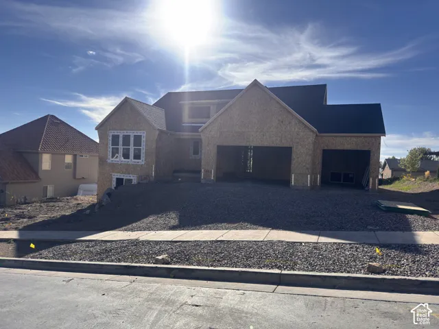 New construction residence with an unfinished exterior, featuring a multi-pane window, dark roof shingles, and a visible two-car garage