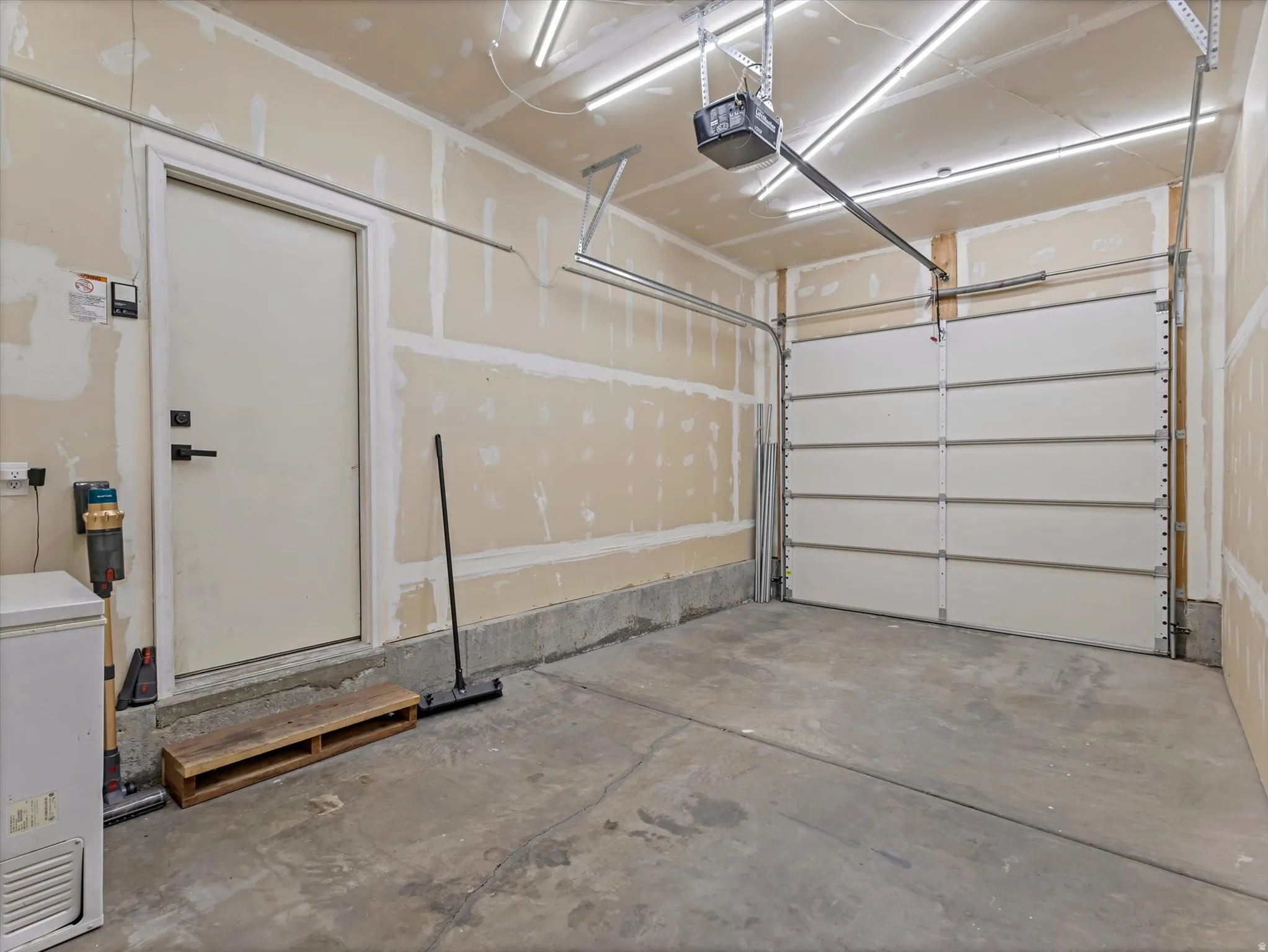 Single-bay garage featuring a concrete floor, an overhead sectional door with opener, a side entry door, and overhead strip lighting