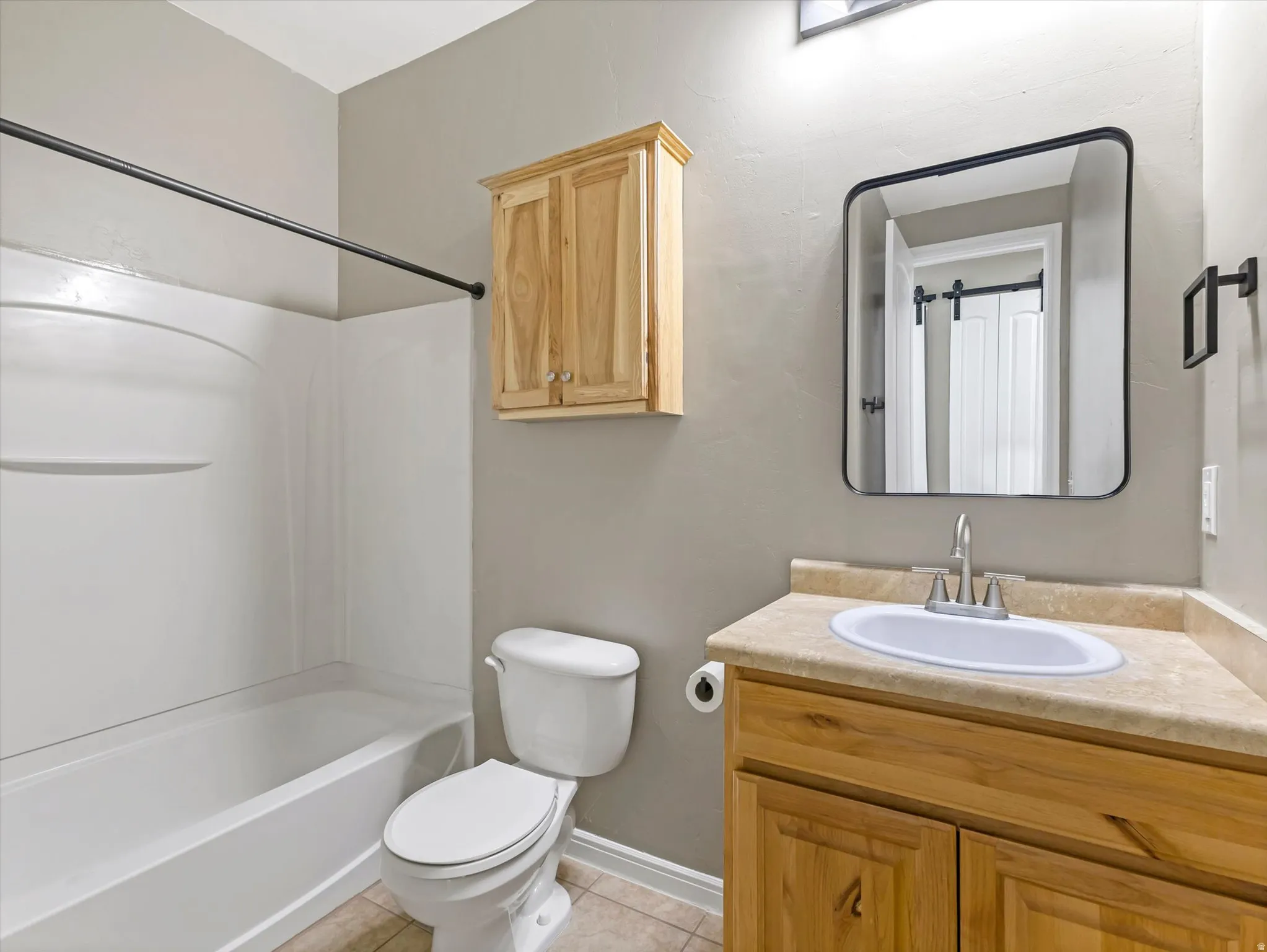 Bathroom featuring a white tub and shower combination, a toilet, and a light wood-finish vanity with a built-in sink