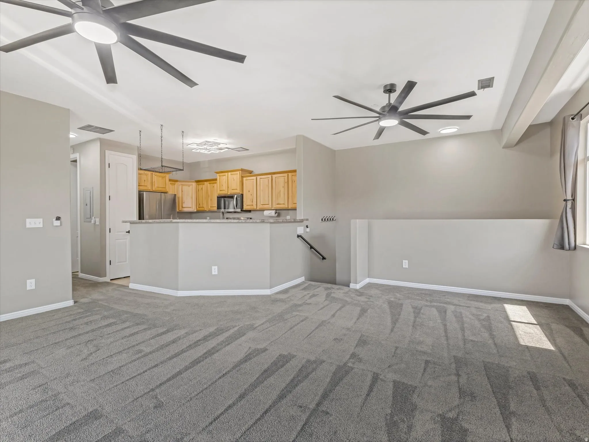 Open-concept living area with gray carpeting and two contemporary ceiling fans