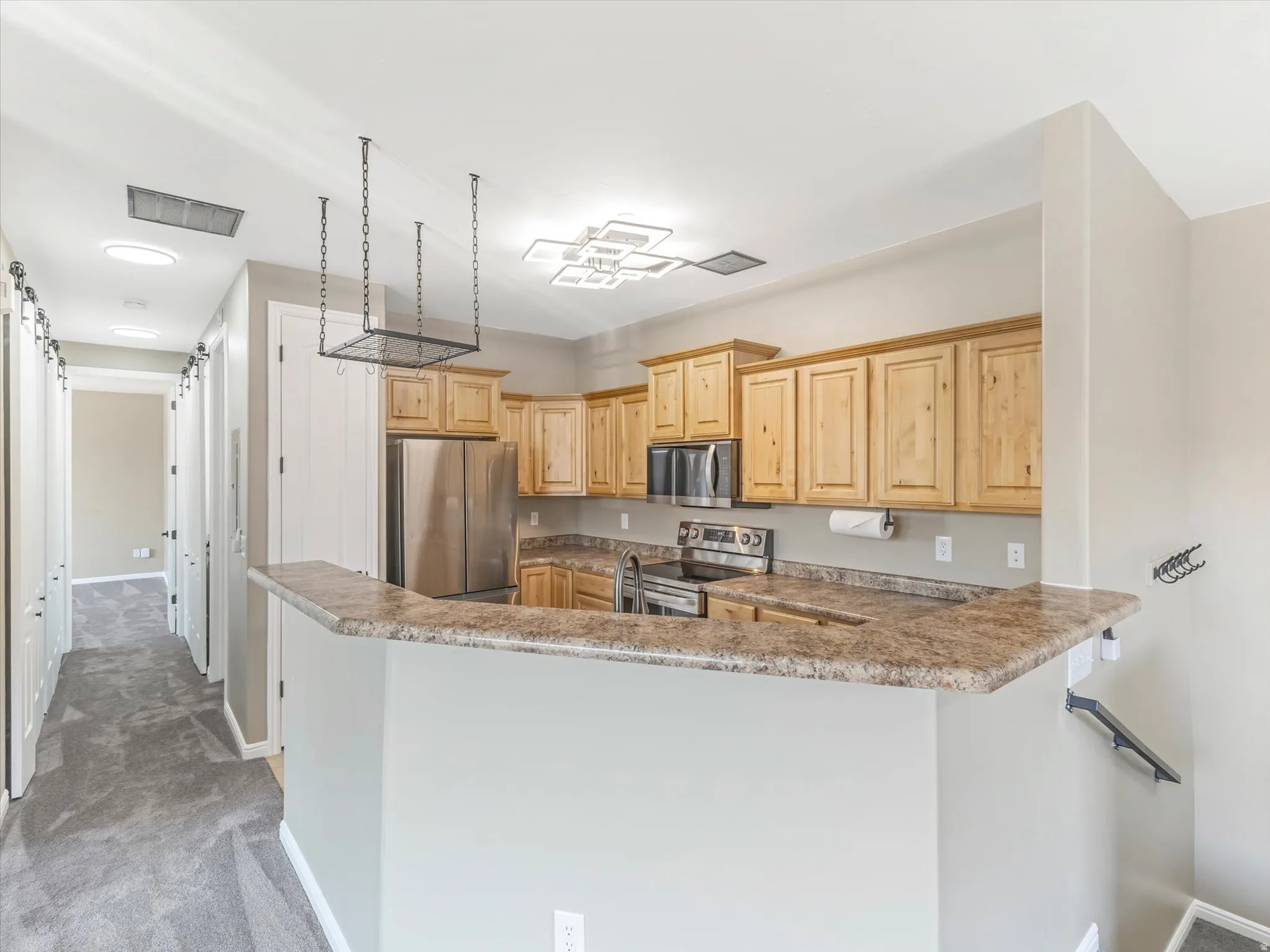 Kitchen featuring light wood cabinetry, stainless steel appliances, a breakfast bar, and a decorative pot rack