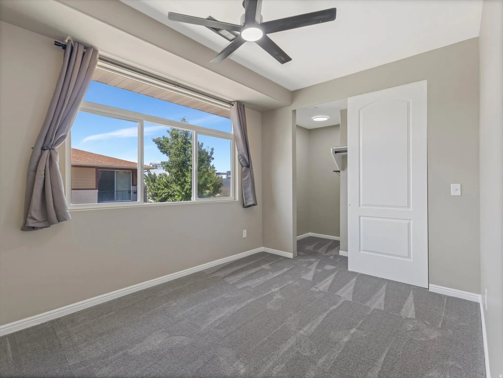 Carpeted room featuring a ceiling fan with integrated lighting, a wide window with sills, a sliding panel door, and built-in closet shelving