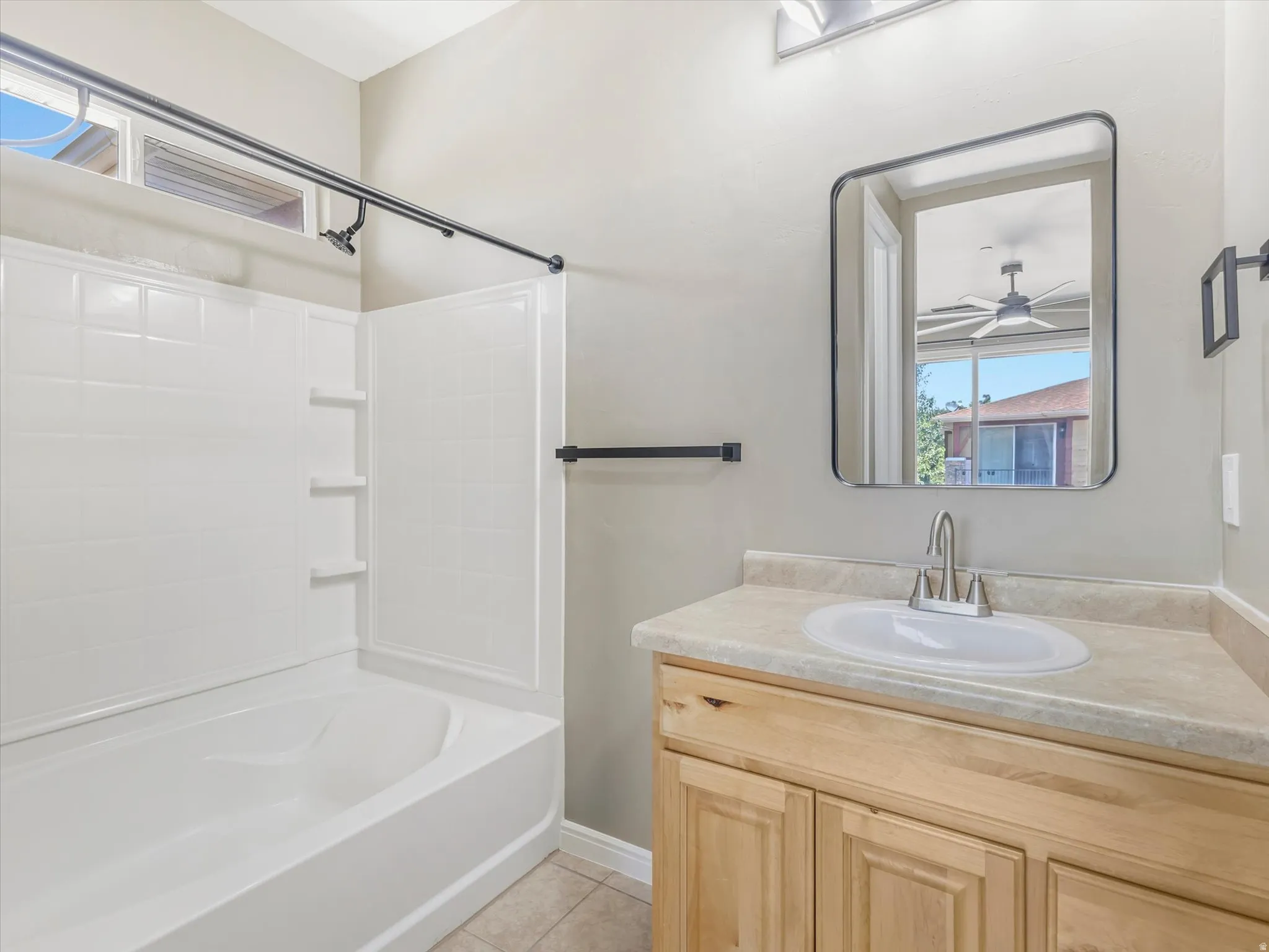 Bathroom featuring a white tub-shower combination with integrated shelving, light wood-finish vanity with an integrated sink, and an oval mirror with a black frame
