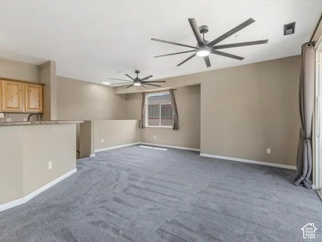 Spacious living area featuring two ceiling fans, carpet flooring, and a window with curtain rods