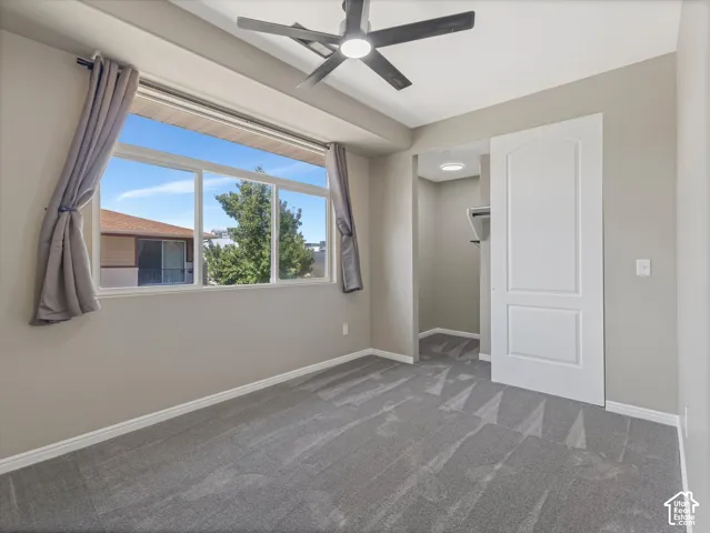 Carpeted room featuring a ceiling fan with integrated lighting, a wide window with sills, a sliding panel door, and built-in closet shelving