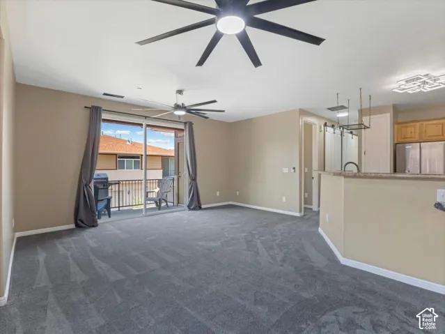 Spacious room featuring gray carpeting, modern ceiling fans, and a sliding glass door opening to a balcony