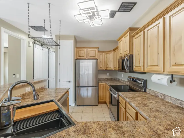 Kitchen featuring light wood cabinetry, stainless steel appliances, speckled countertops, and a contemporary ceiling light fixture