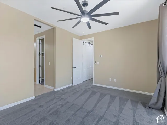 Plush grey carpet flooring, modern ceiling fan, white paneled doors, and tan wall finishes