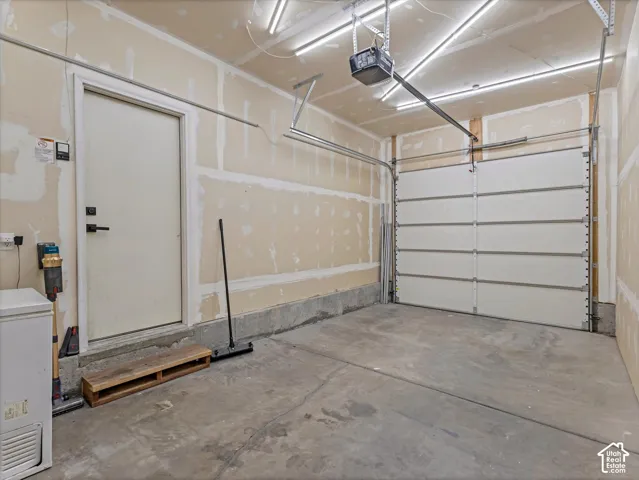 Single-bay garage featuring a concrete floor, an overhead sectional door with opener, a side entry door, and overhead strip lighting