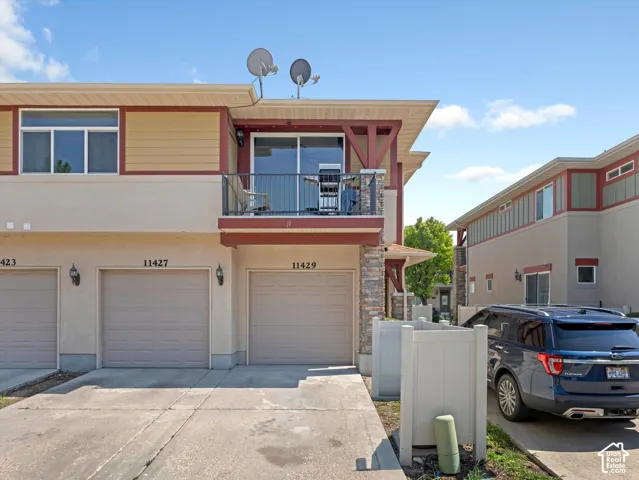 Multi-level exterior with stucco and siding, featuring a private balcony with metal railing, an attached garage, and a concrete driveway