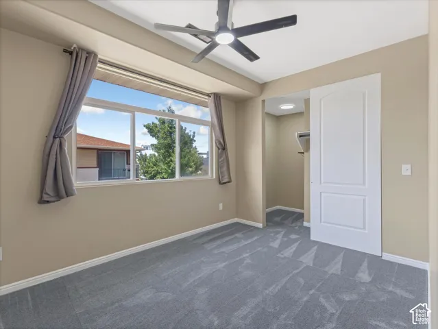 Recessed window with a multi-pane design, neutral wall color, grey patterned carpeting, ceiling fan with integrated lighting, and a white sliding door