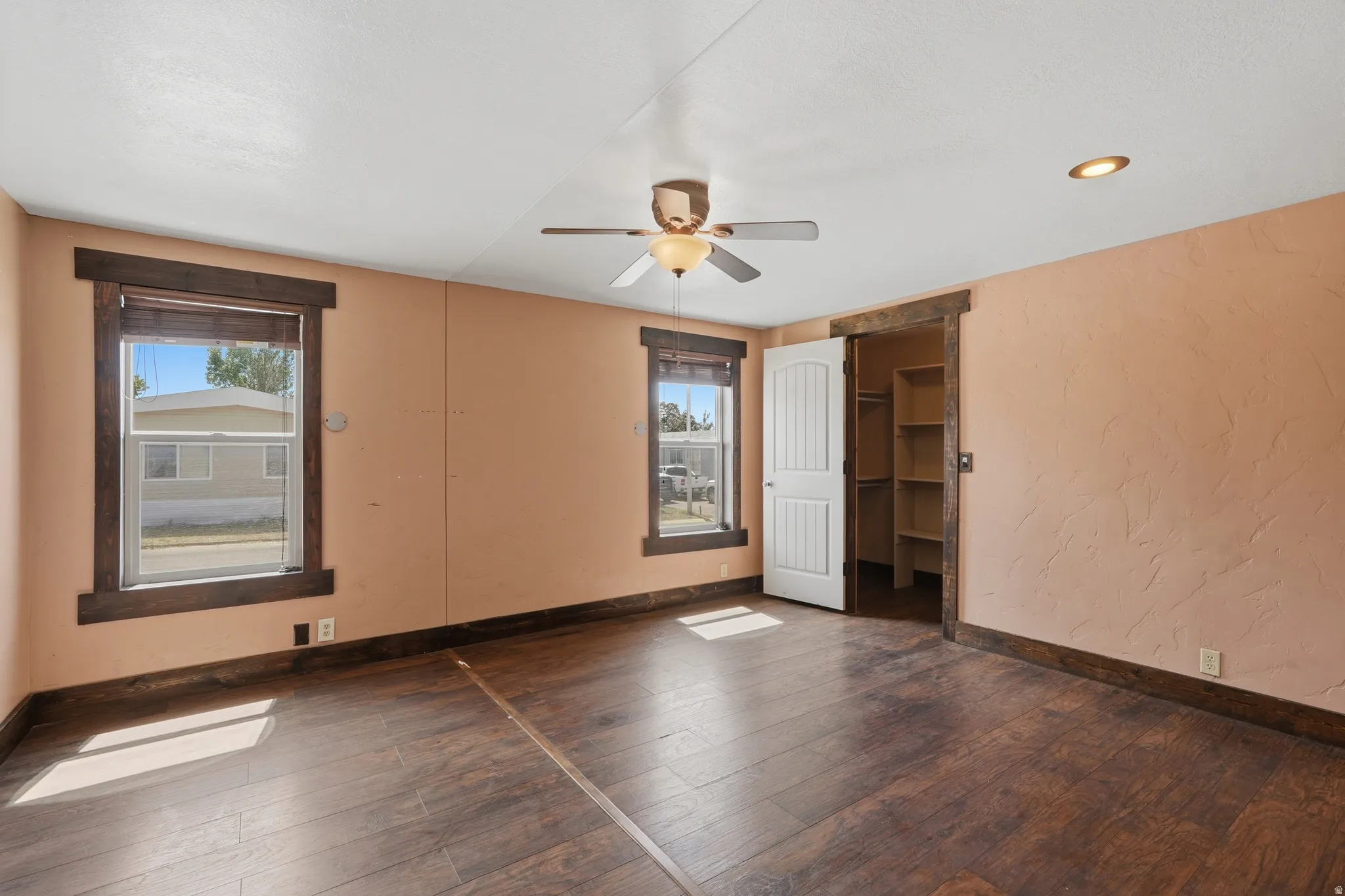 Room featuring rich wood-finish flooring, textured peach walls, and dark wood trim