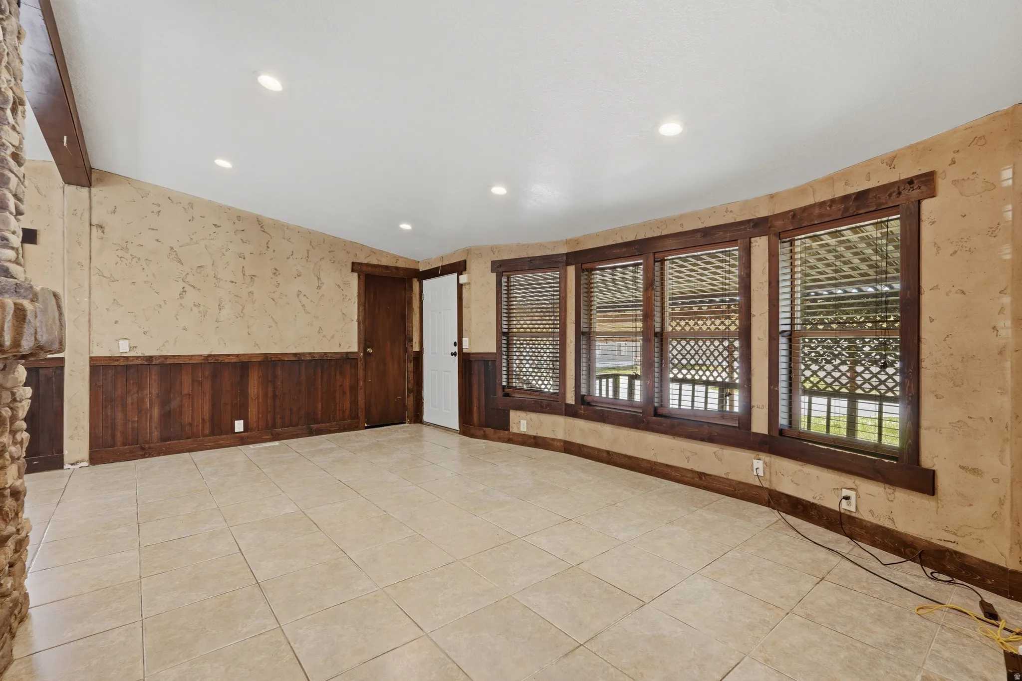 Spacious interior featuring neutral tile flooring, wood paneling, textured wall finishes, recessed lighting, and multiple windows with wood blinds