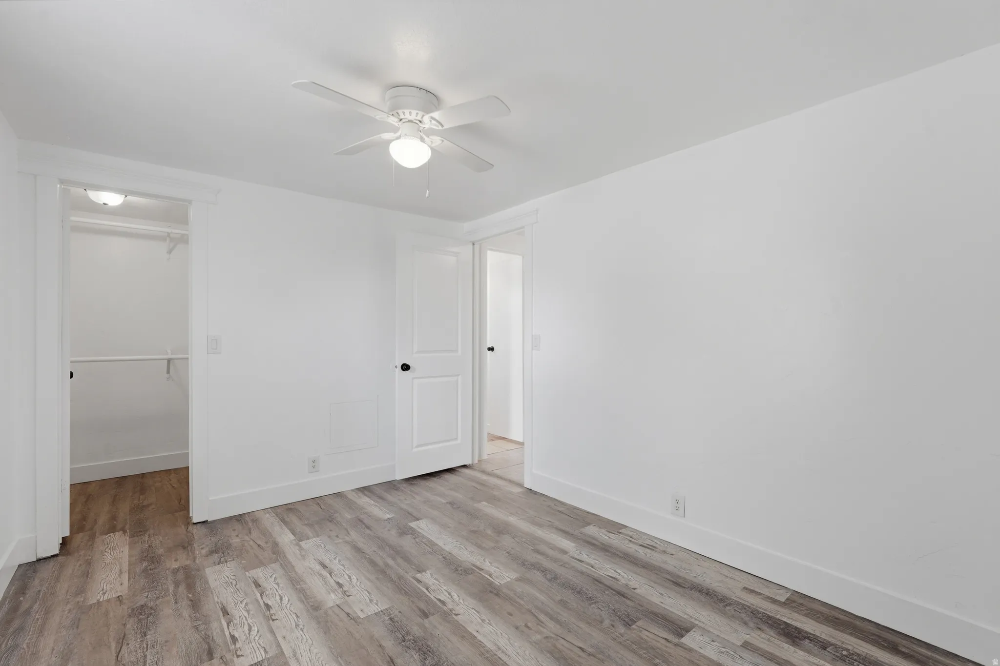 Interior room featuring wood-finish flooring, white walls, and a white ceiling fan with integrated lighting