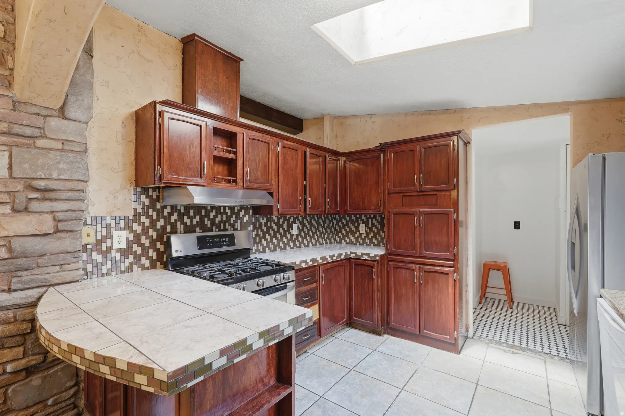 Kitchen featuring wood cabinetry, stainless steel range, patterned tile backsplash, and a skylight