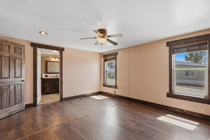 Spacious room featuring wood-finish flooring, two large windows with dark wood trim, a ceiling fan with integrated lighting, and a recessed ceiling light