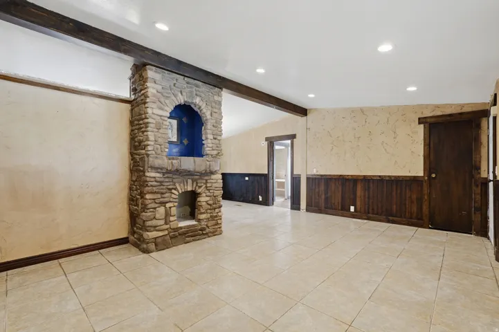Stone-clad fireplace with an arched niche, tile flooring, wood paneling, and exposed ceiling beams