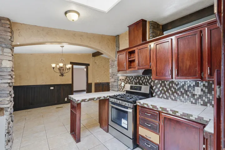 Kitchen featuring stainless steel range, wood cabinetry, patterned tile backsplash, and tile countertops