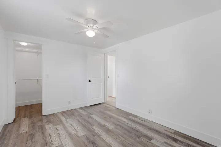 Interior room featuring wood-finish flooring, white walls, and a white ceiling fan with integrated lighting