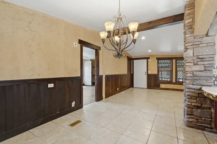 Open-concept living area featuring light-toned tile flooring, wainscoting with a dark wood finish, and a decorative chandelier
