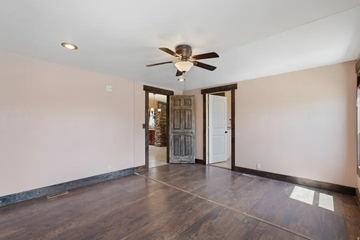 Spacious room featuring wood-finish flooring, a ceiling fan with integrated lighting, recessed lighting, and dark wood trim