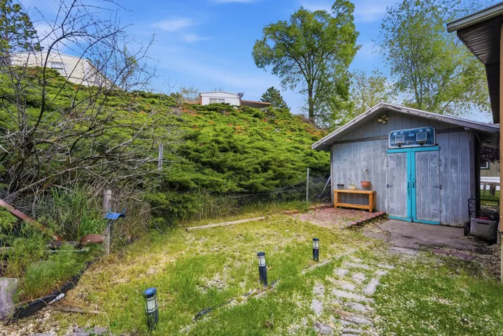 Backyard area featuring a detached wooden shed with a painted door, a stone paver pathway, and a sloped, natural landscape with established ground cover