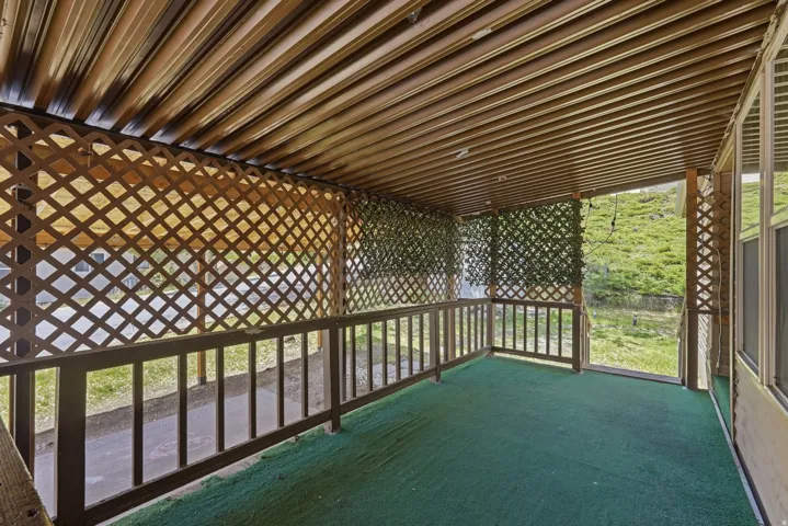 Covered porch featuring a slatted wood ceiling, lattice fencing, a wood railing, and green outdoor carpeting