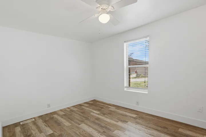 Bright interior space featuring wood-finish flooring, a single window with blinds, and a white ceiling fan with integrated lighting