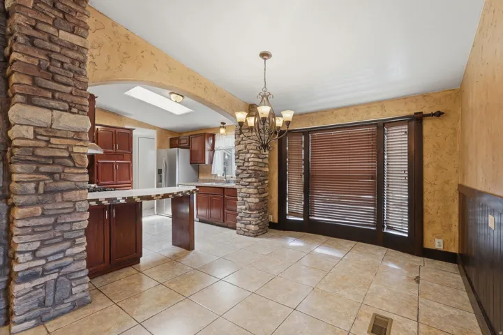Kitchen and dining area featuring stone columns, tile flooring, rich wood cabinetry, a breakfast bar, and a skylight