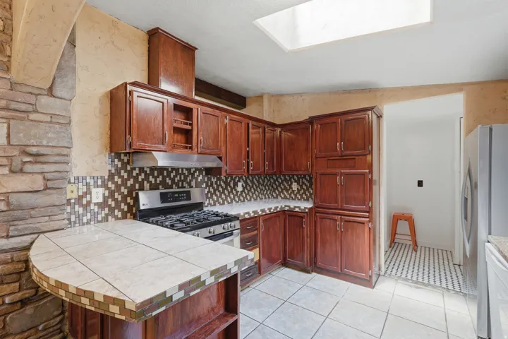 Kitchen featuring wood cabinetry, stainless steel range, patterned tile backsplash, and a skylight