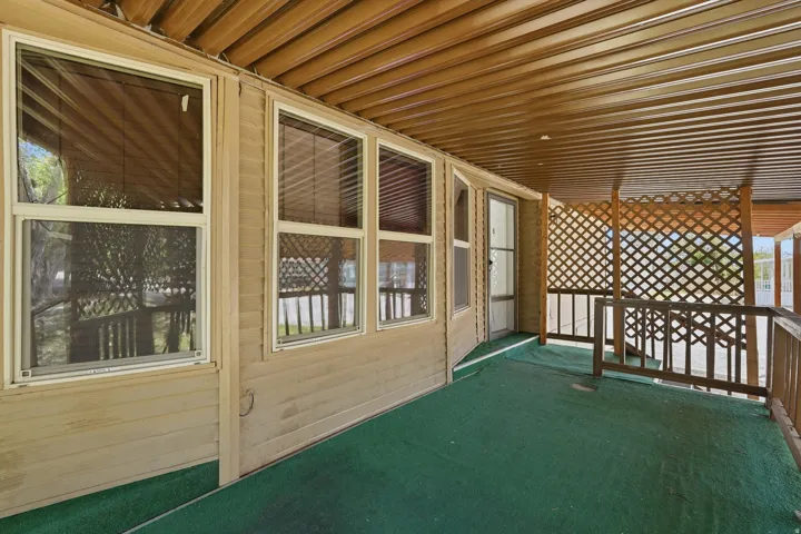 Covered patio area featuring a green artificial turf floor, lattice privacy screening, multiple windows with blinds, and a paneled ceiling