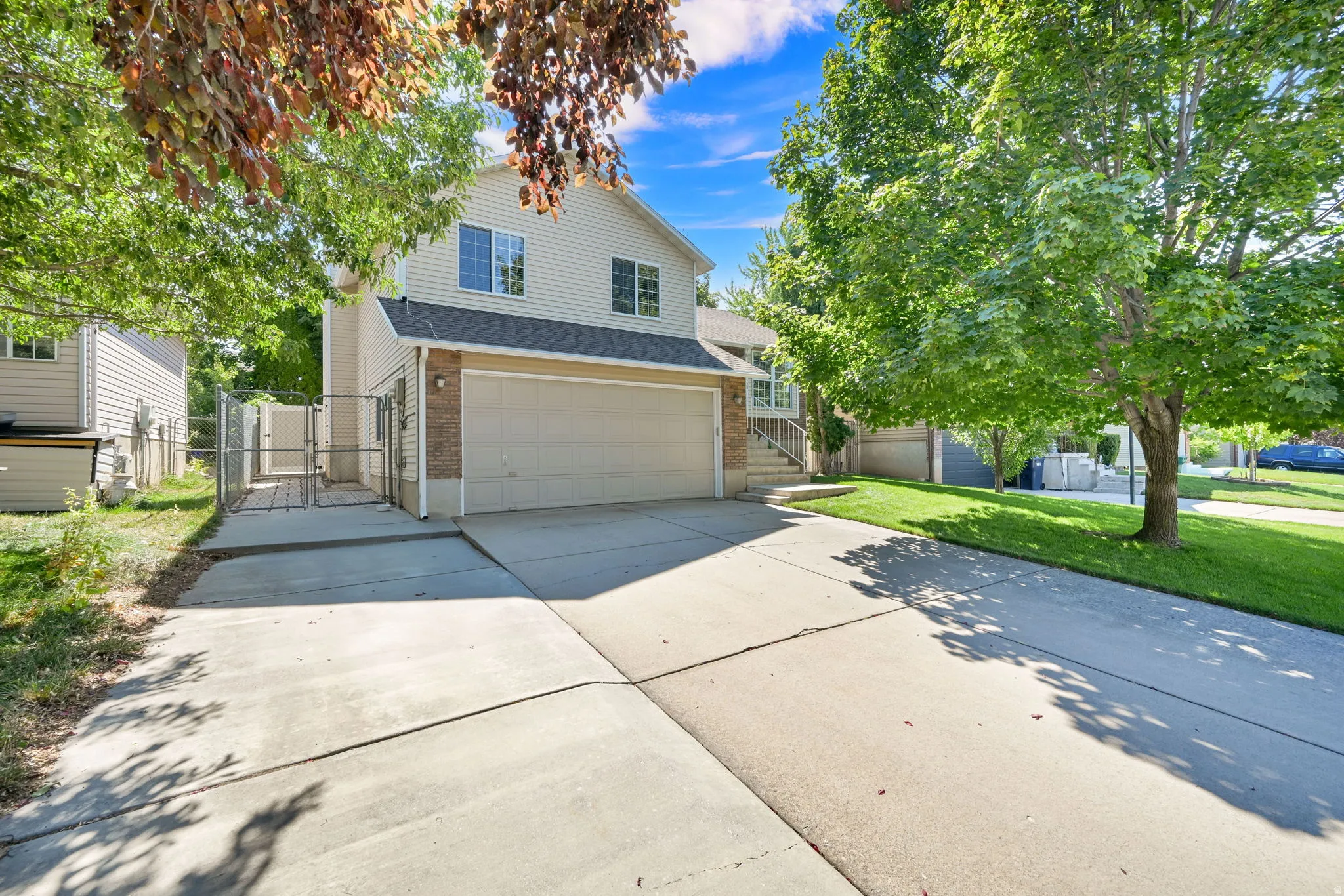 Two-story home featuring a spacious driveway with concrete apron, two-car attached garage with neutral-toned door, and mature landscaping with established trees providing natural shade