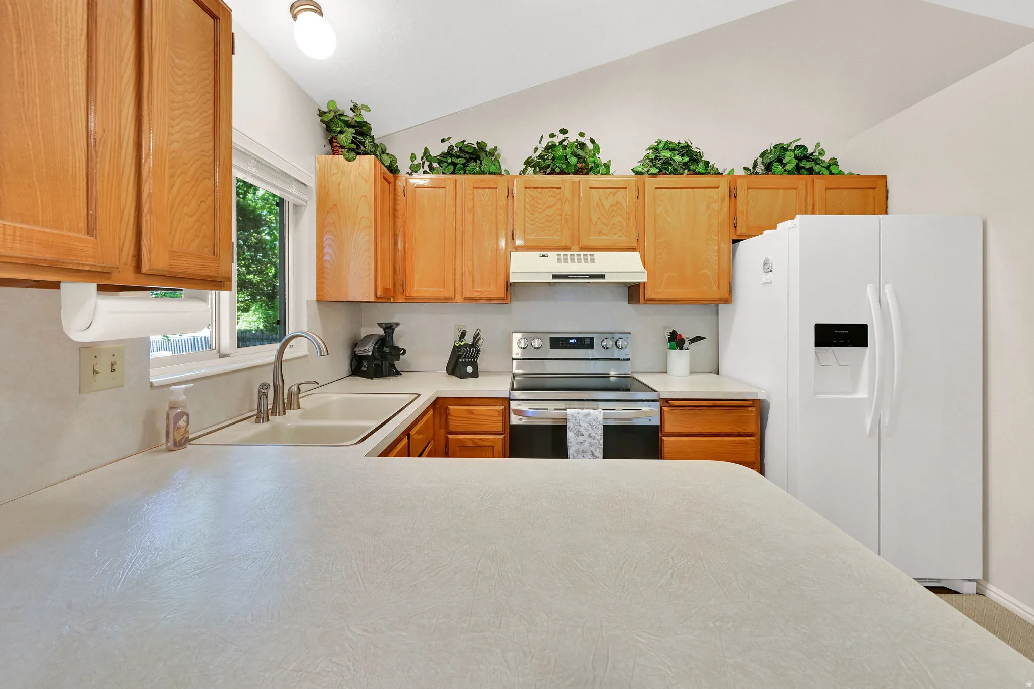 Kitchen featuring wood cabinetry, light countertops, stainless steel appliances, and a vaulted ceiling