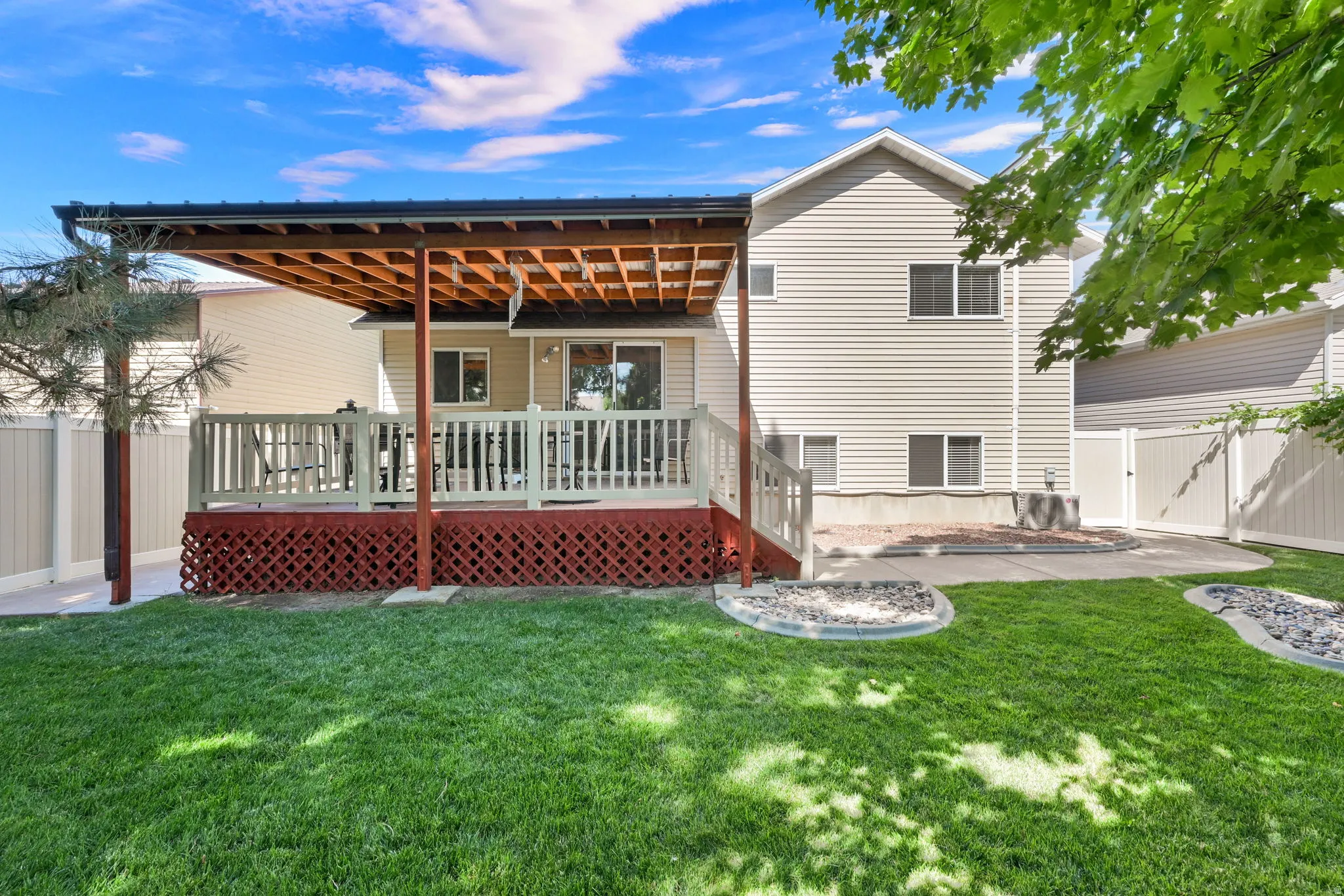 Spacious backyard featuring a covered wood deck, expansive lawn, and concrete patio