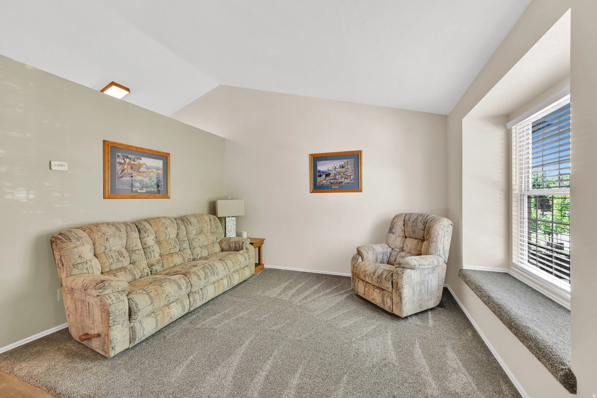 Bright, naturally lit living room featuring a large bay window with plantation shutters, neutral wall finishes, and plush carpeting