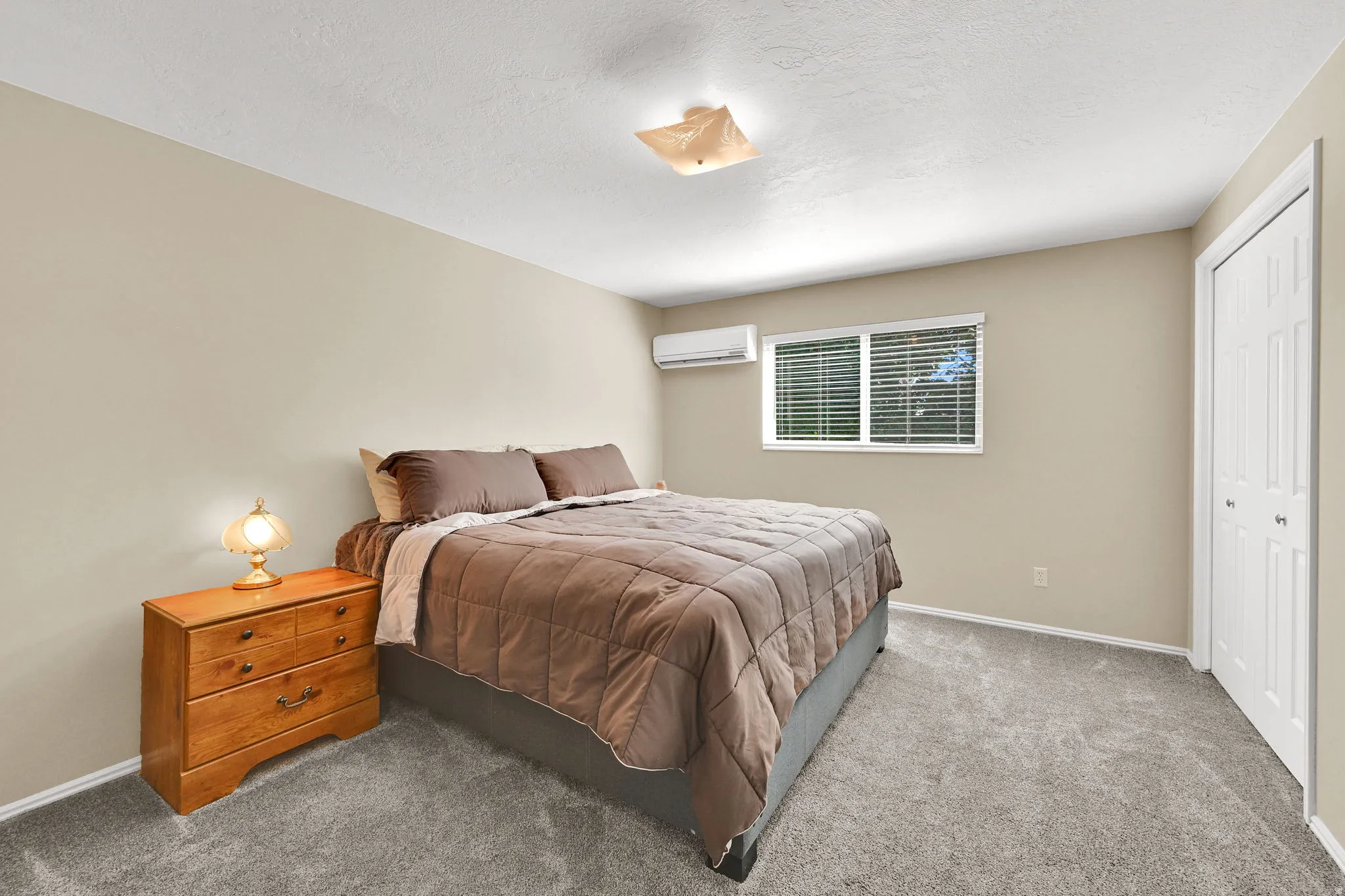 Carpeted room featuring a window with horizontal blinds, neutral wall paint, and a wall-mounted air conditioning unit