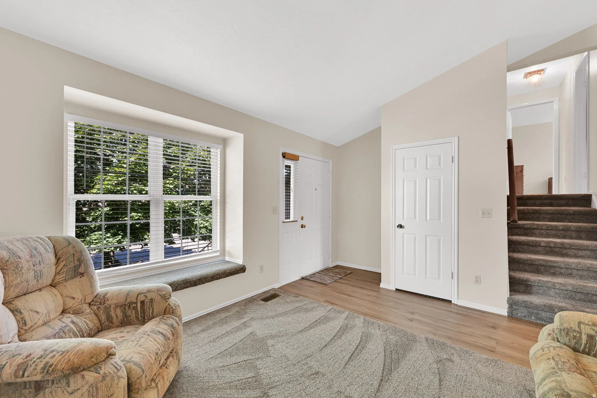 Entry area featuring a large window with blinds, wood-finish flooring, a six-panel interior door, and a carpeted staircase