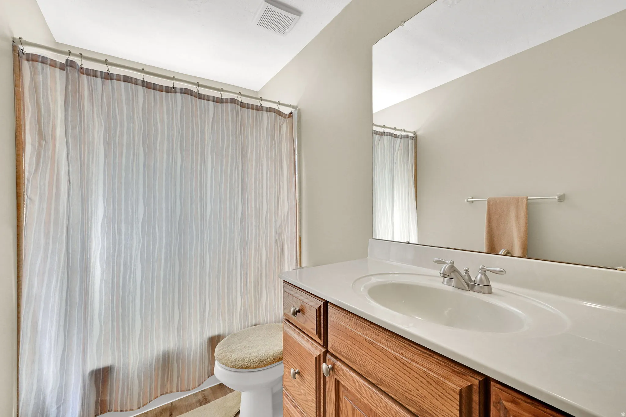 Bathroom featuring a wood-finish vanity with an integrated sink and brushed nickel faucet, a large frameless mirror, and a ceiling-mounted ventilation fan