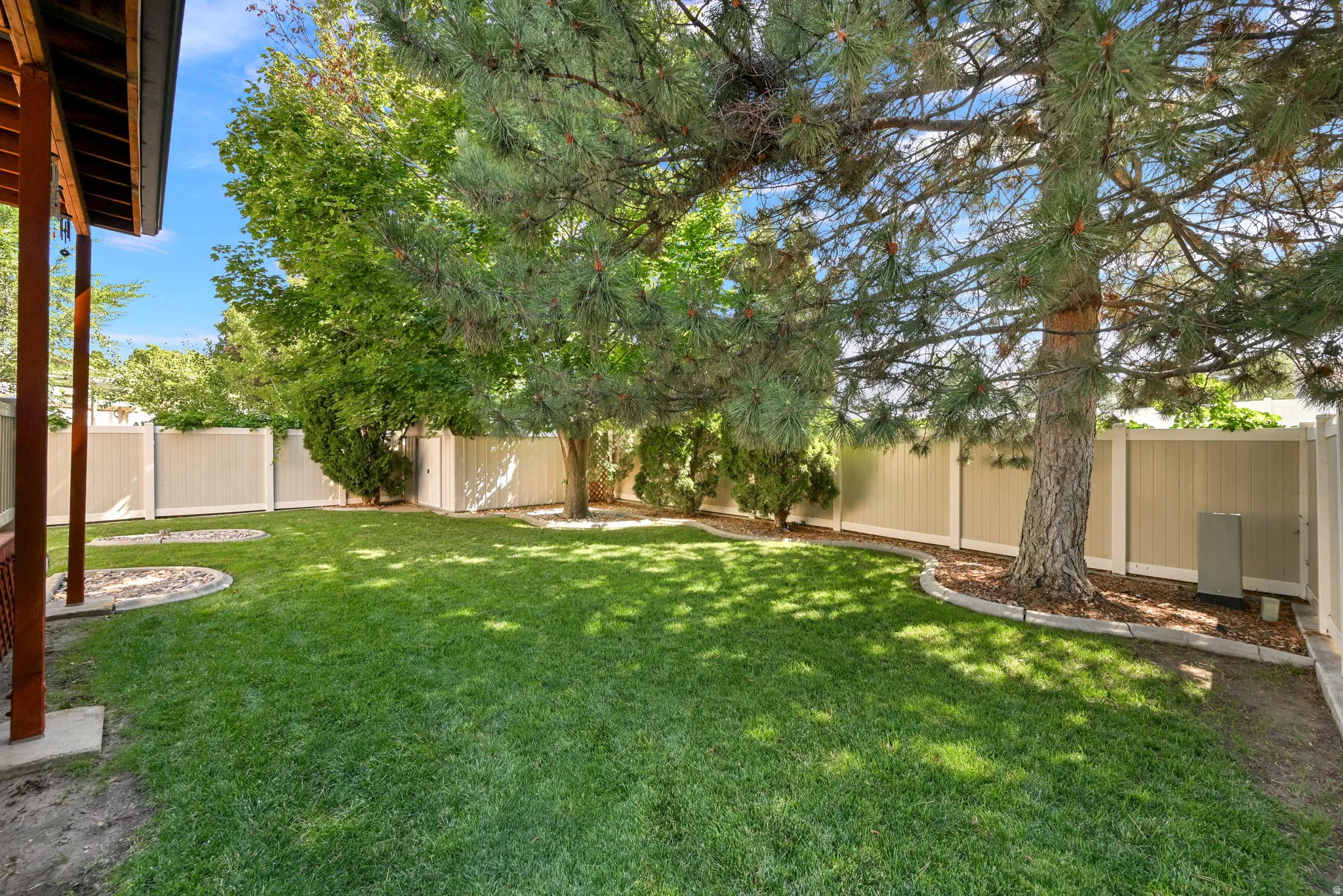 Expansive backyard featuring a lush green lawn, mature trees providing natural shade, and full perimeter fencing