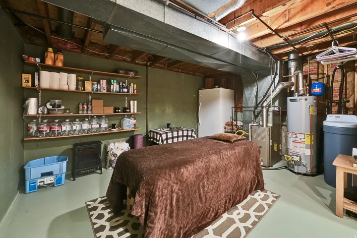 Basement space featuring exposed ceiling joists and ductwork, a water heater, furnace, and water softener system