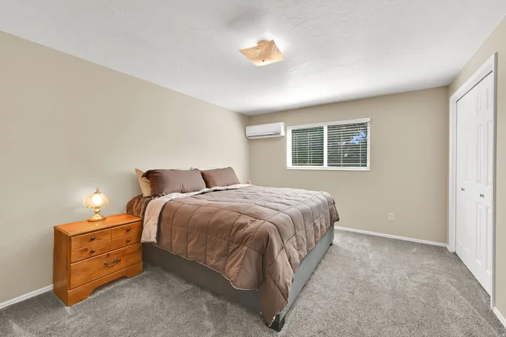 Carpeted room featuring a window with horizontal blinds, neutral wall paint, and a wall-mounted air conditioning unit