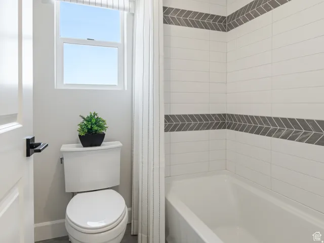 Bathroom featuring a white subway tile surround with a decorative chevron accent band, a white bathtub, and a window with blinds
