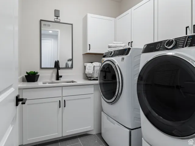 Laundry area featuring white cabinetry, a countertop with an undermount sink, and modern appliances