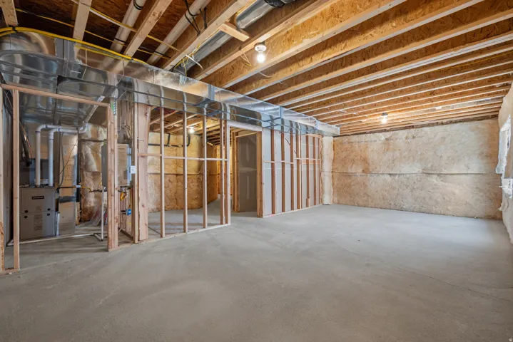 Unfinished basement space featuring exposed wood joists and subflooring, concrete flooring, and partial wood framing
